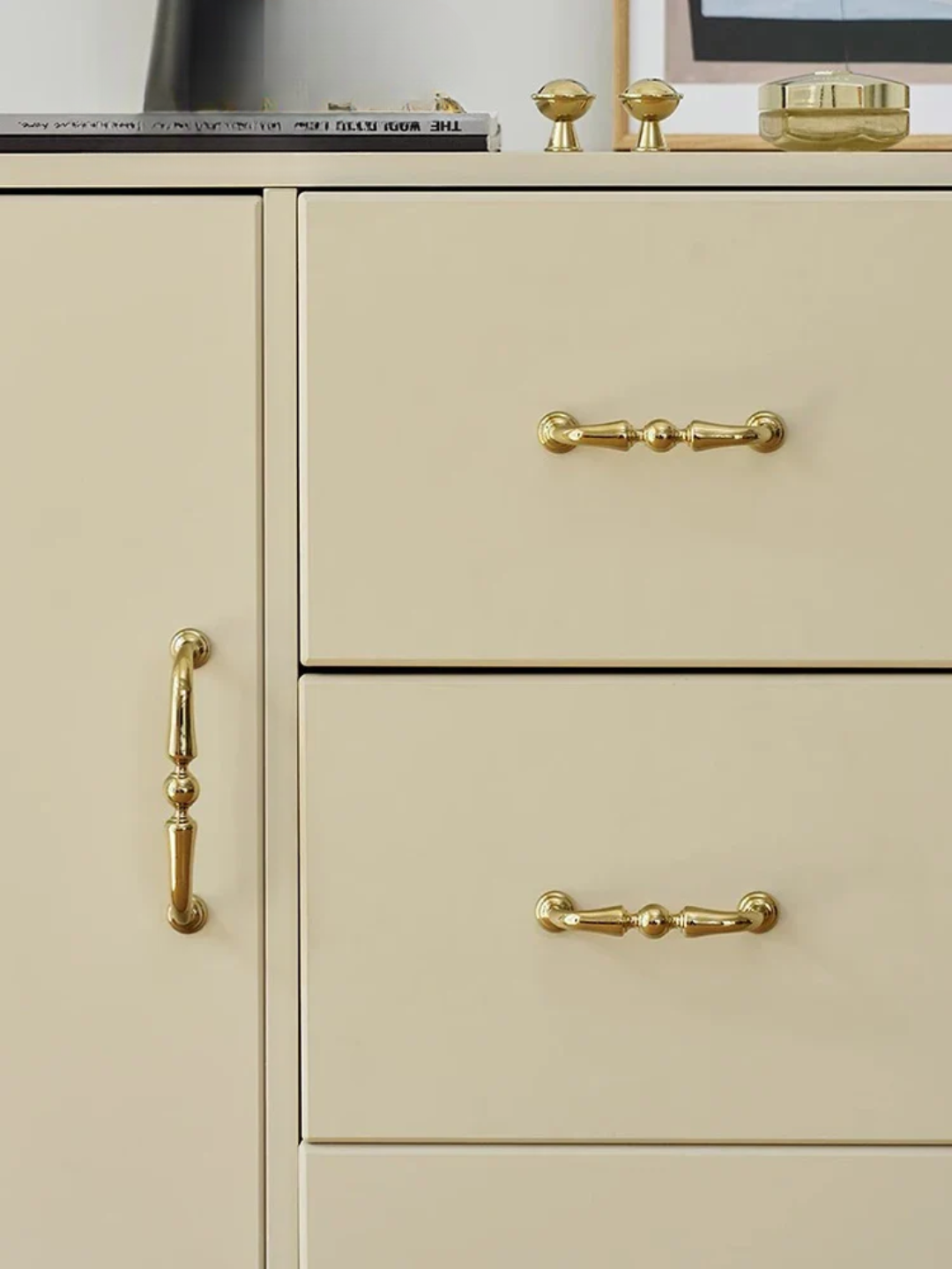 Beige cabinet with gold handles and knobs on a neutral background
