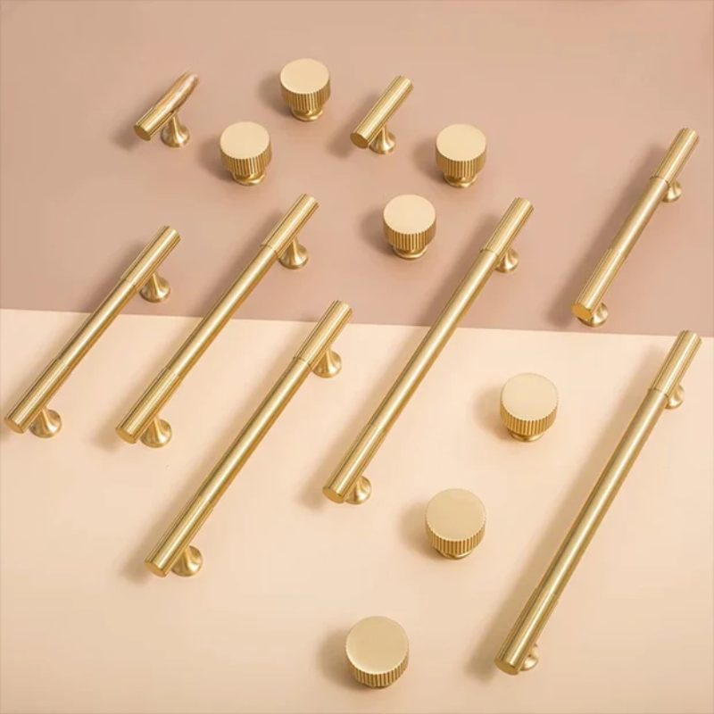 Collection of gold cabinet handles and knobs on a beige background