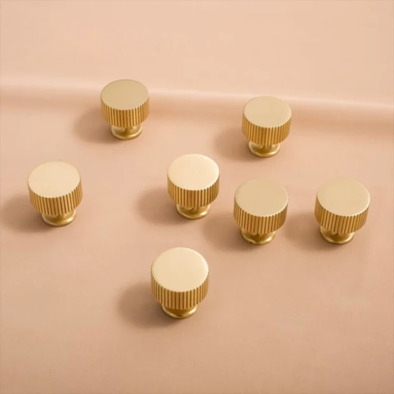 Collection of gold cabinet handles and knobs on a beige background