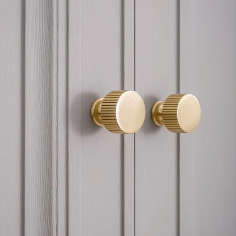 Two gold cabinet knobs on a gray wooden panel