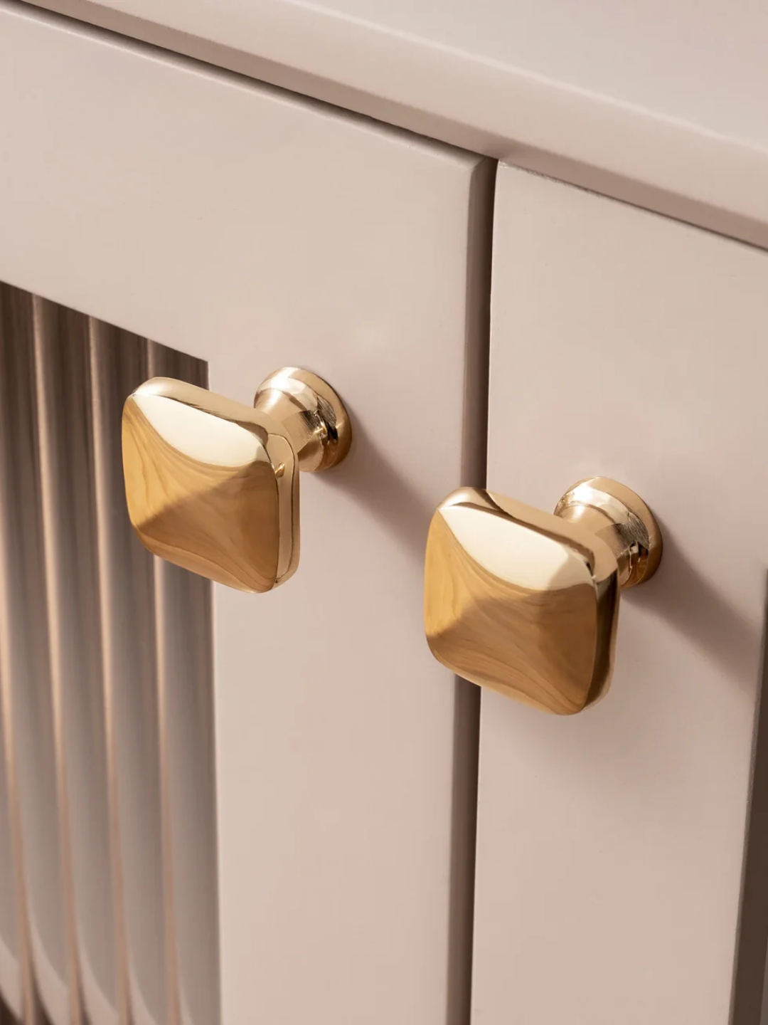 Close-up of gold cabinet knobs on a light-colored wooden cabinet.