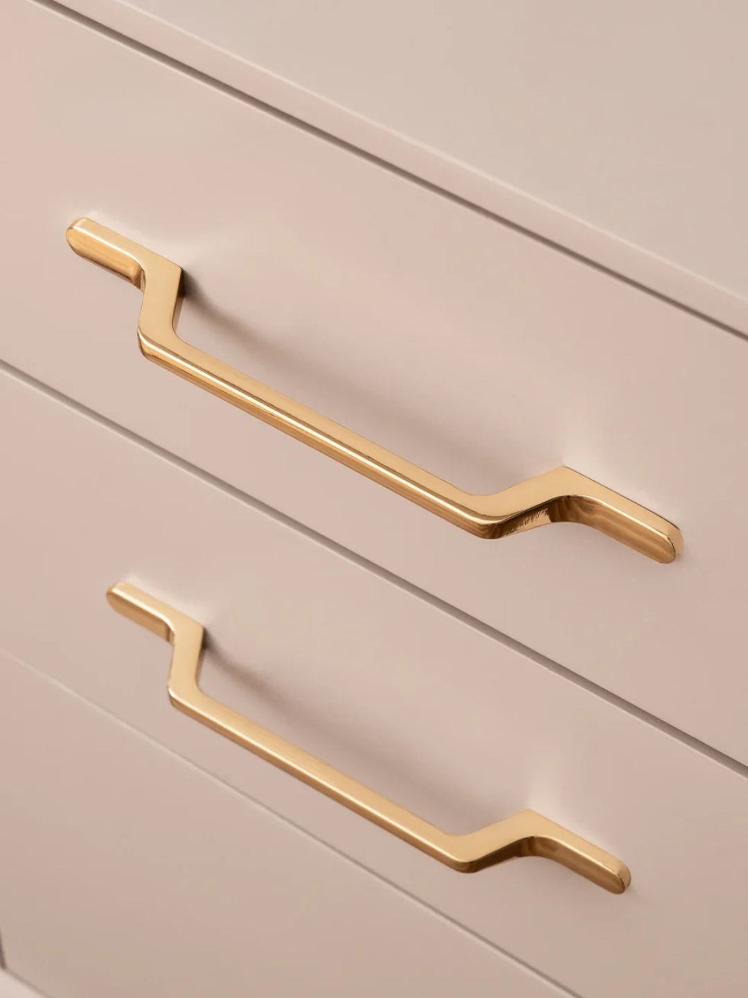 Two gold handles on a light gray cabinet.