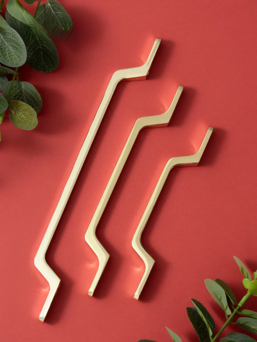Three gold metal straws on a red background with green leaves.