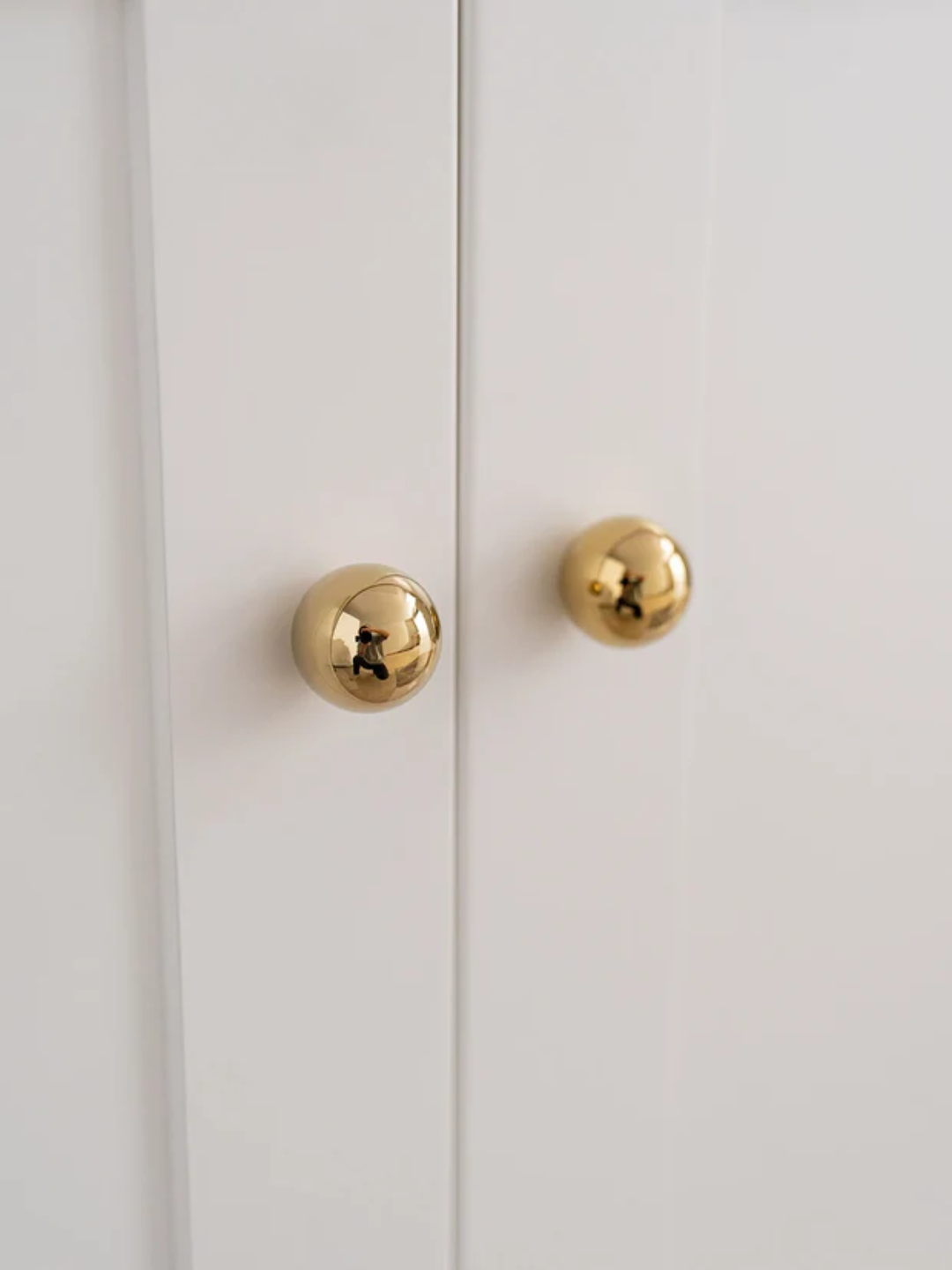 Gold spherical door handles on a green and white door.