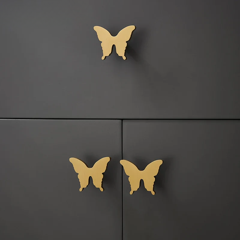 Butterfly-shaped gold cabinet knobs on a black cabinet.