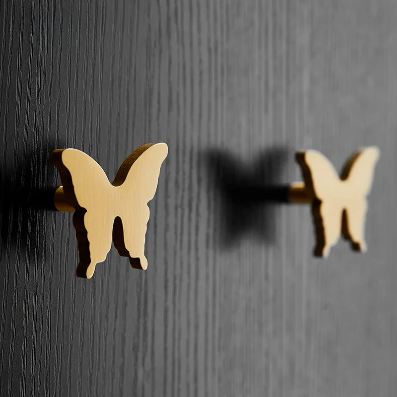 Gold butterfly-shaped cabinet handles on a black cabinet.