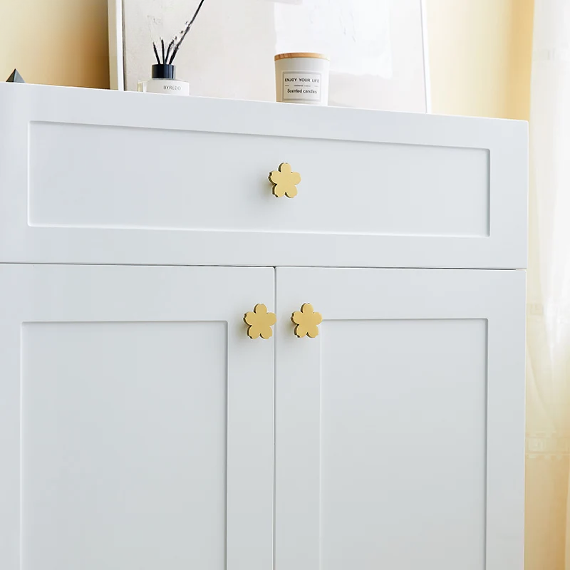 White cabinet with gold flower-shaped handles in a neutral setting