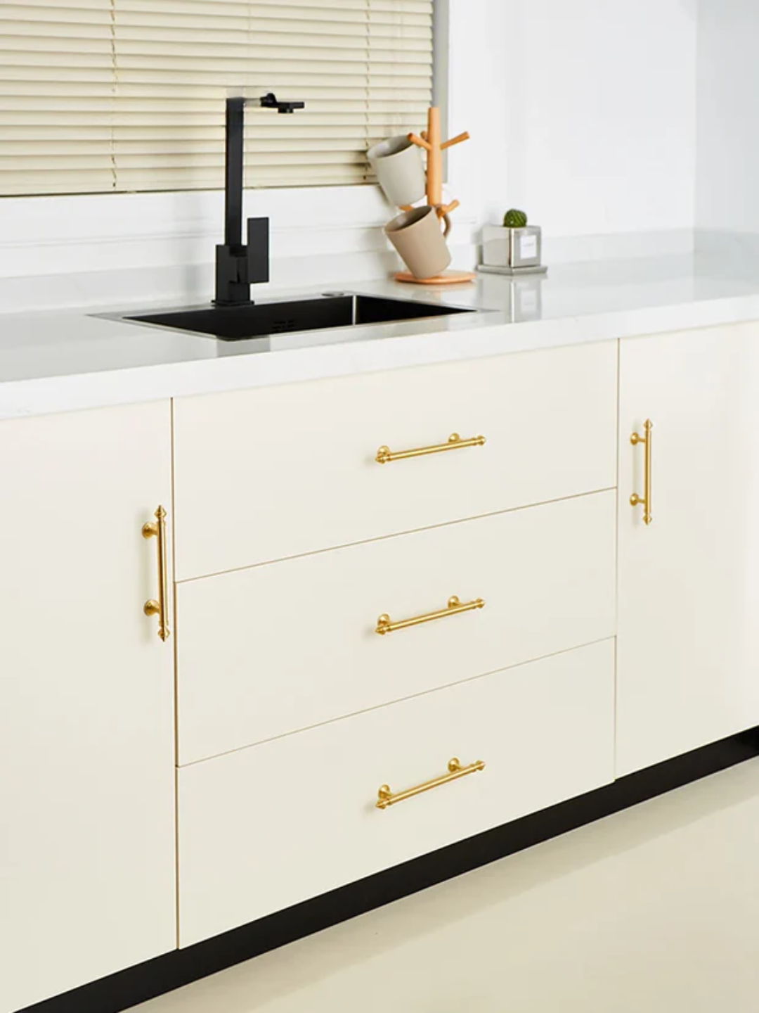 Modern kitchen with white cabinets, gold handles, and a black sink.