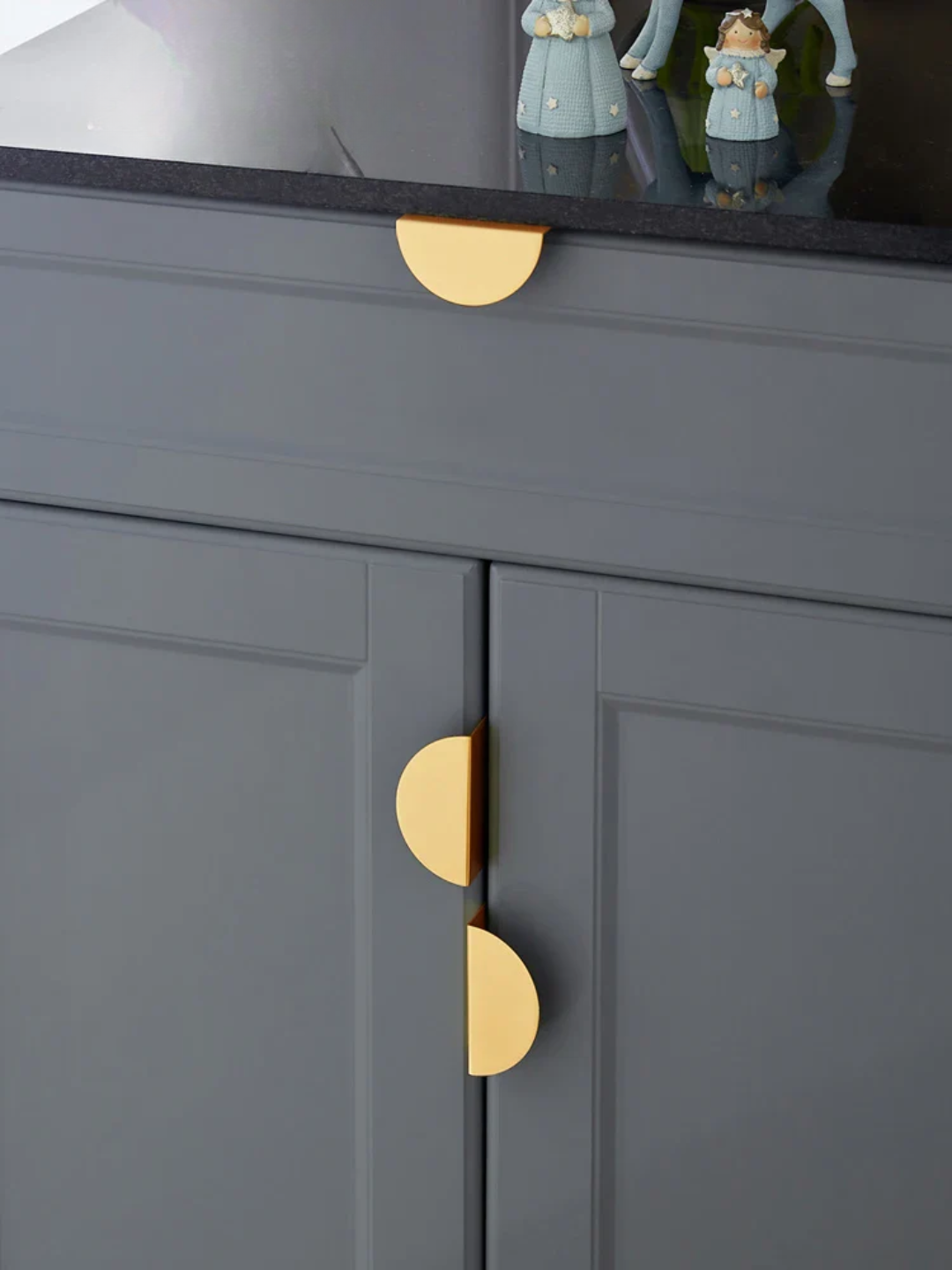 Gray cabinet with gold handles and decorative figurines on a reflective surface