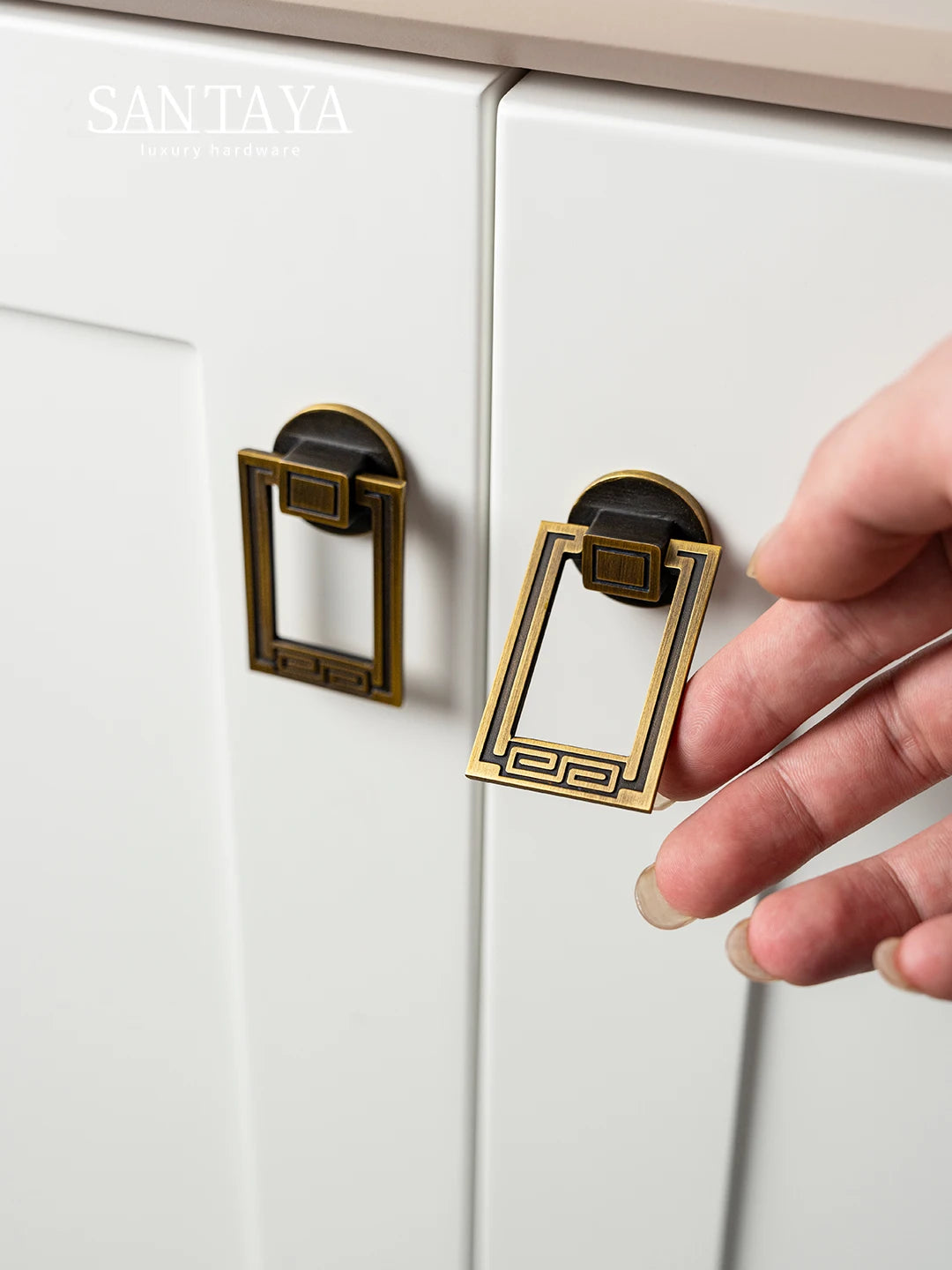 Hand holding a gold cabinet handle against a white cabinet.