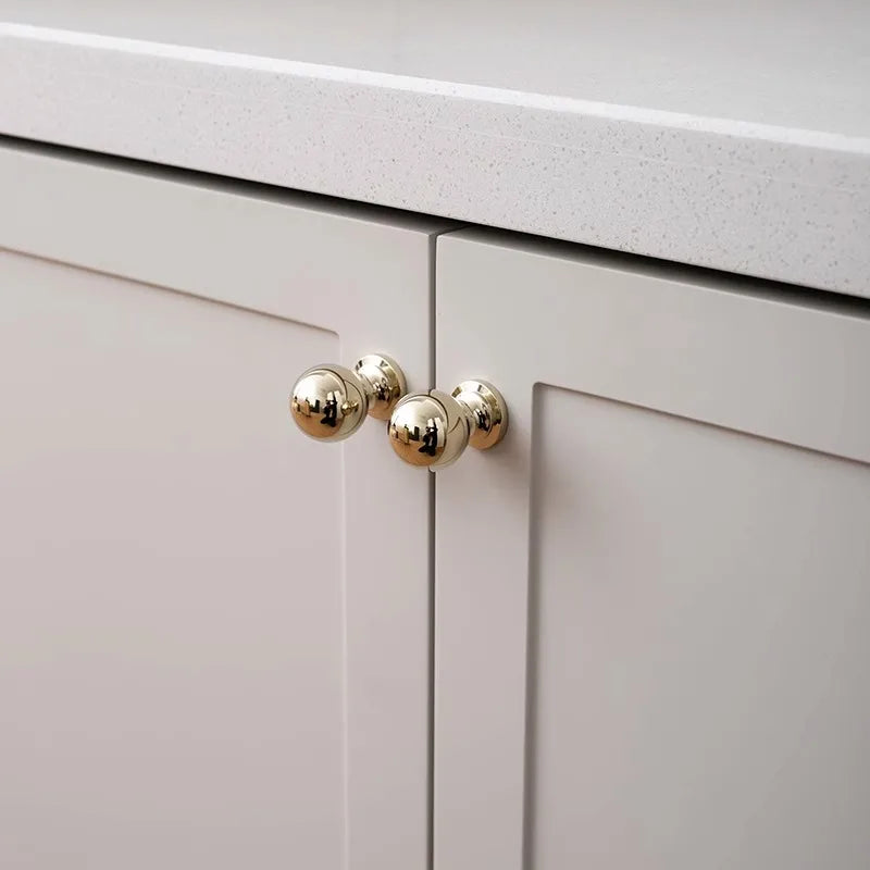Close-up of a light gray cabinet with gold knobs.