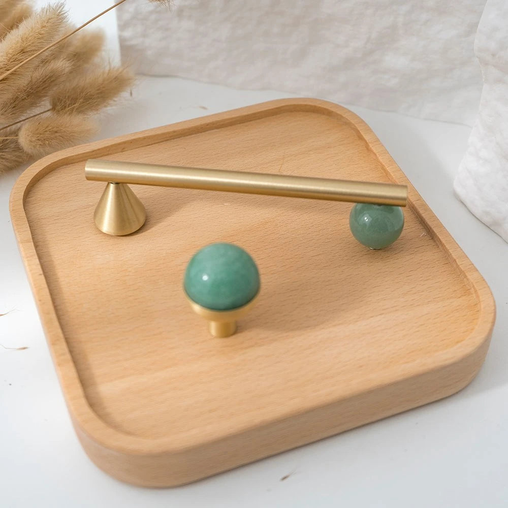 Green decorative cabinet knob with a brass pull on a wood tray