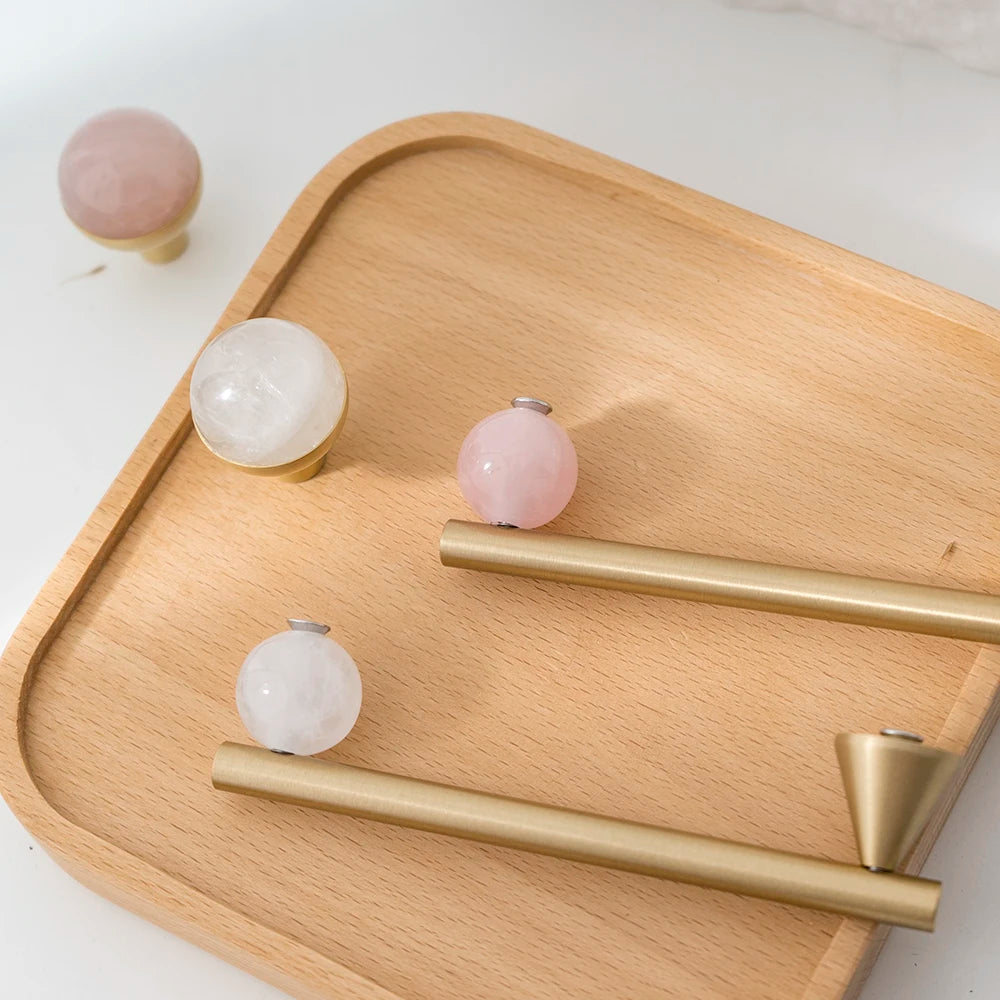 Pink and white decorative cabinet knobs with brass pulls on a wood tray