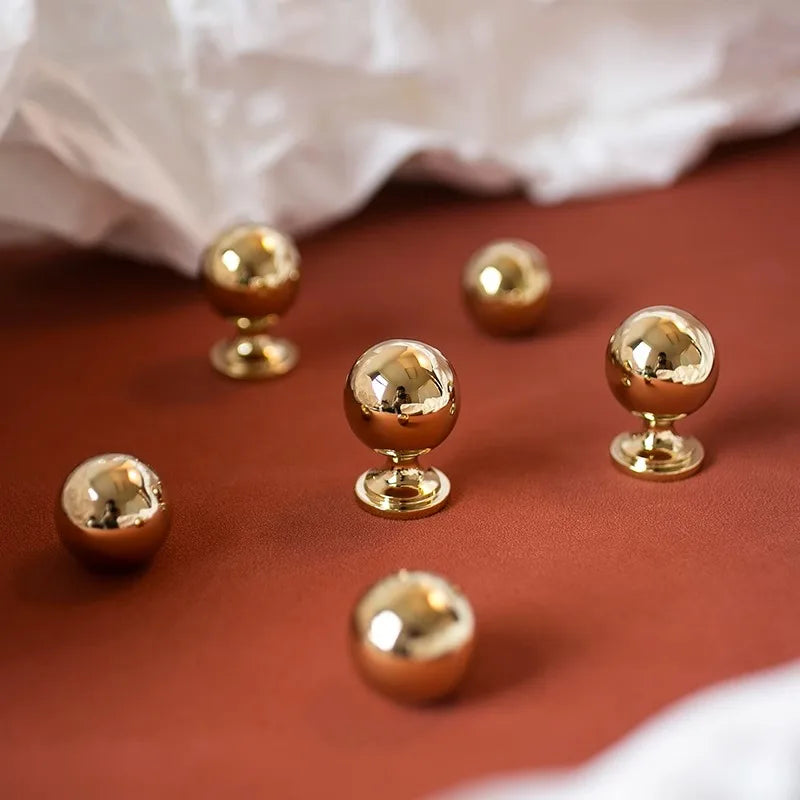 Four gold spherical knobs on a white surface with a red background