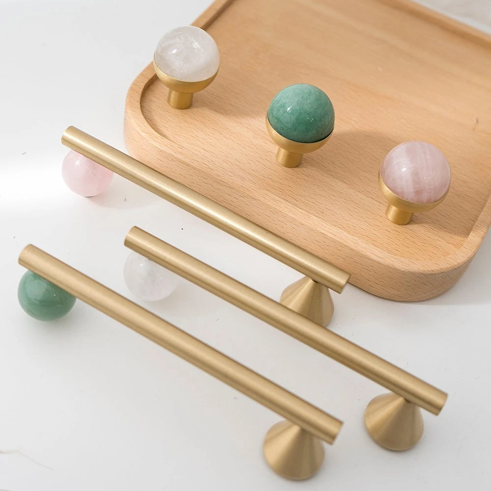 Assorted brass cabinet knobs and pulls in green, pink, and white