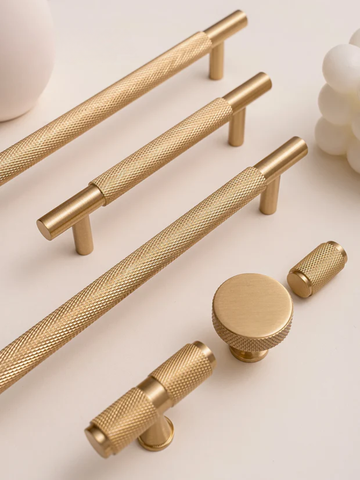 Collection of gold cabinet handles and knobs on a light background
