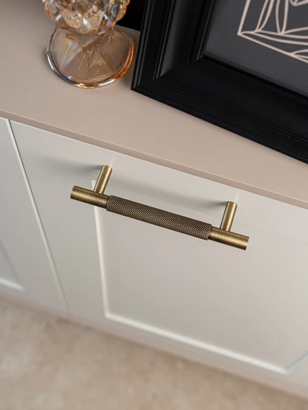 Brass cabinet handle on a white cabinet with a beige countertop.