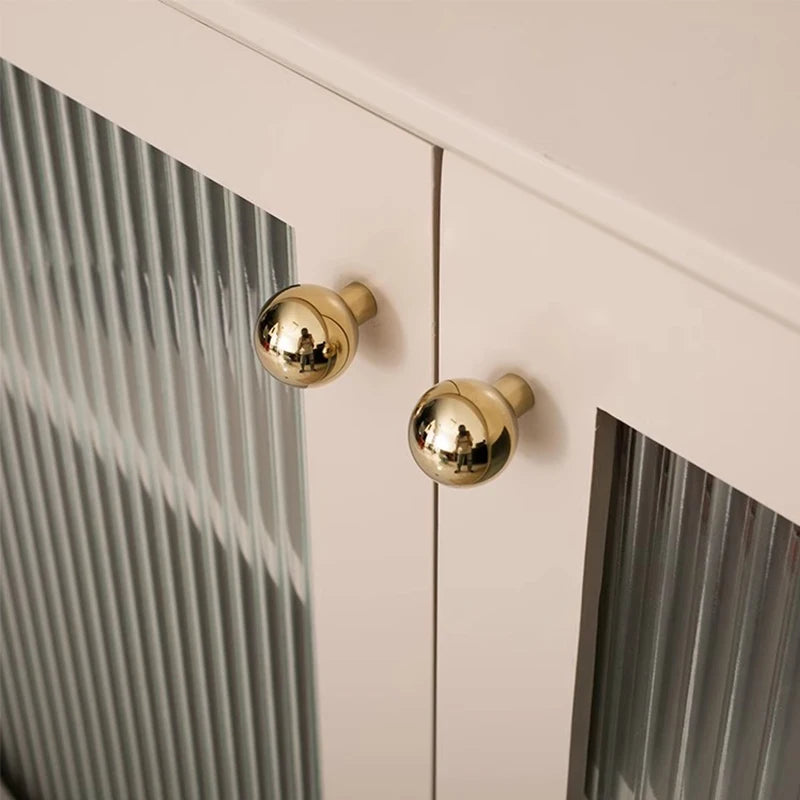 Close-up of a cabinet with gold knobs on a light-colored wall.