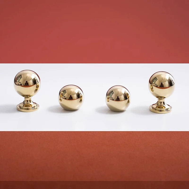 Four gold spherical knobs on a white surface with a red background