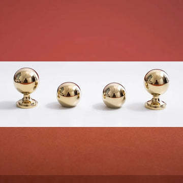 Four gold spherical knobs on a white surface with a red background