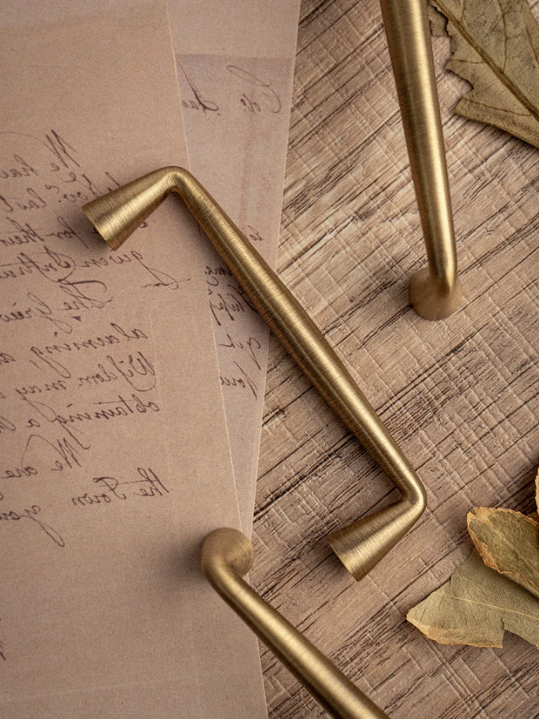 Gold cabinet handles on a textured surface with a piece of paper and leaves.