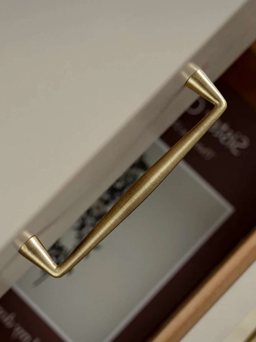 Close-up of a gold cabinet handle on a white cabinet with a blurred background