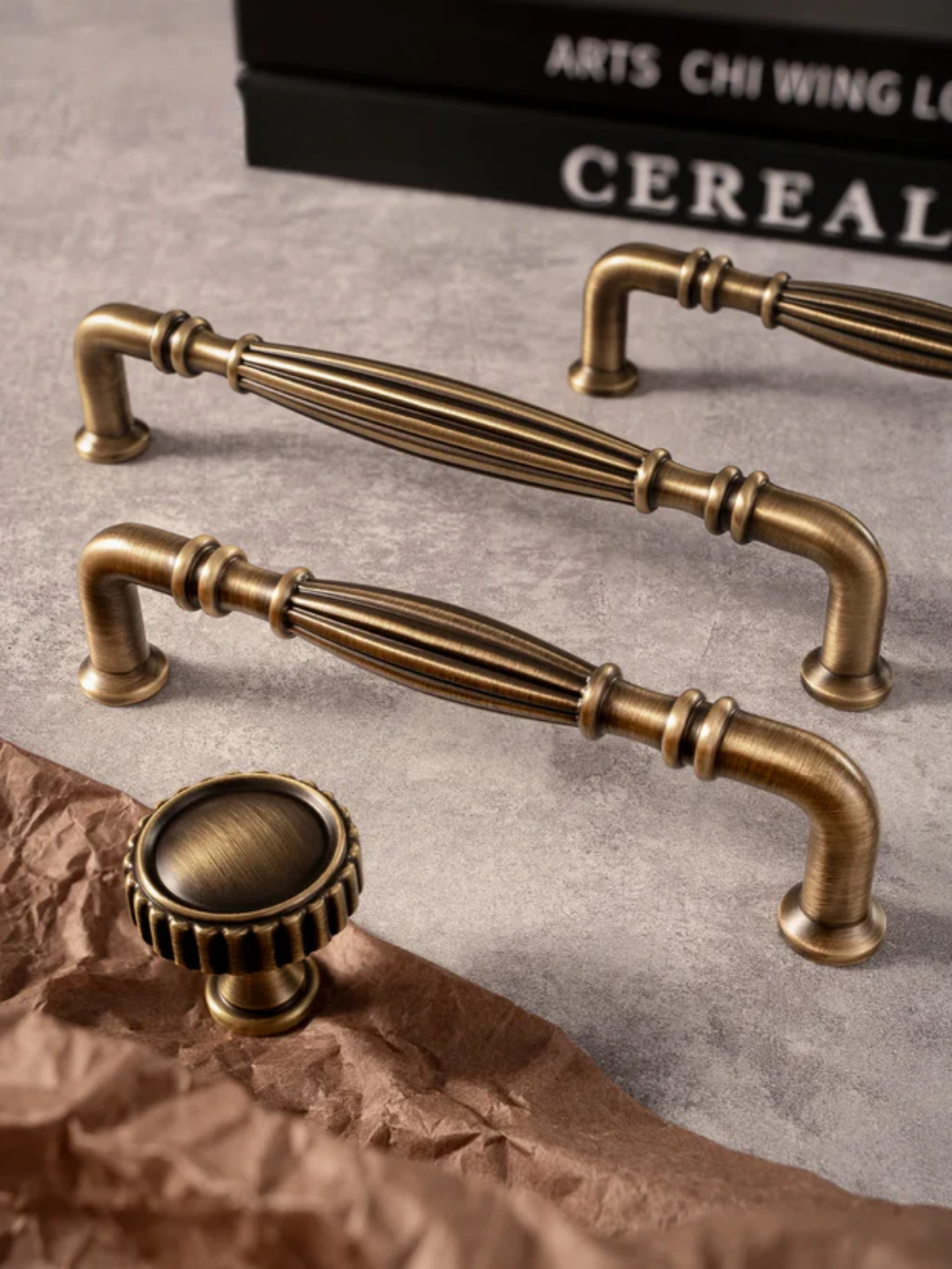 Bronze cabinet handles on a textured surface with a box labeled 'Cereal' in the background.