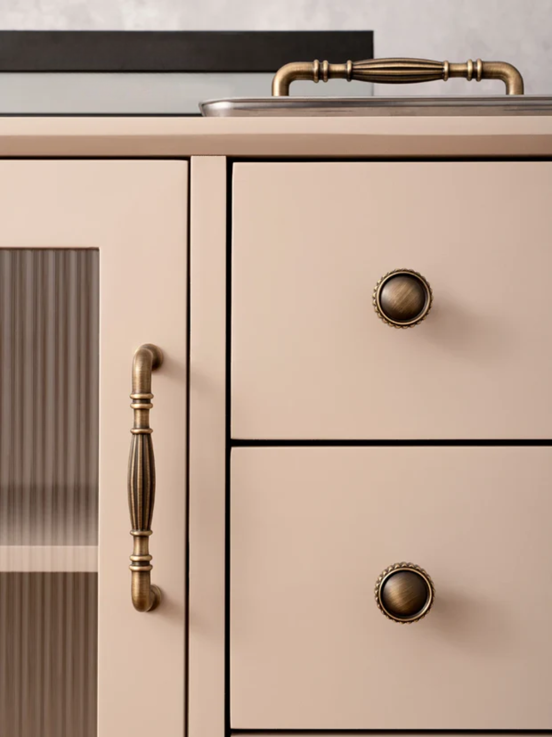 Beige kitchen cabinet with brass handles and knobs on a neutral background