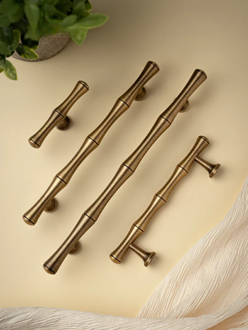 Set of five gold cabinet handles on a beige surface with a plant in the corner.