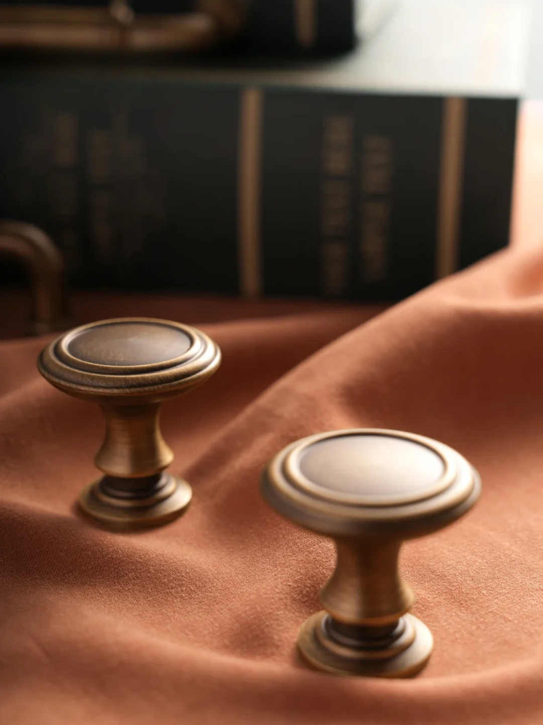 Two bronze cabinet knobs on a brown leather surface with a blurred book in the background.