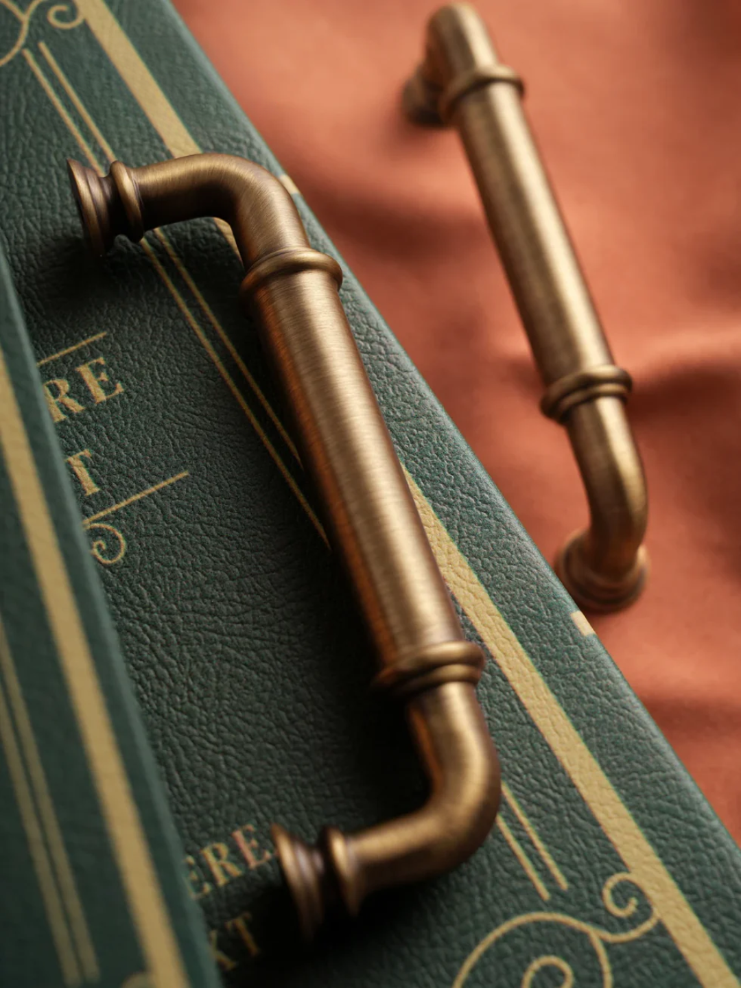 Brass cabinet handles on a green leather-bound book with gold lettering.