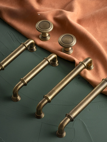 Set of brass cabinet handles on a dark surface with a brown fabric background