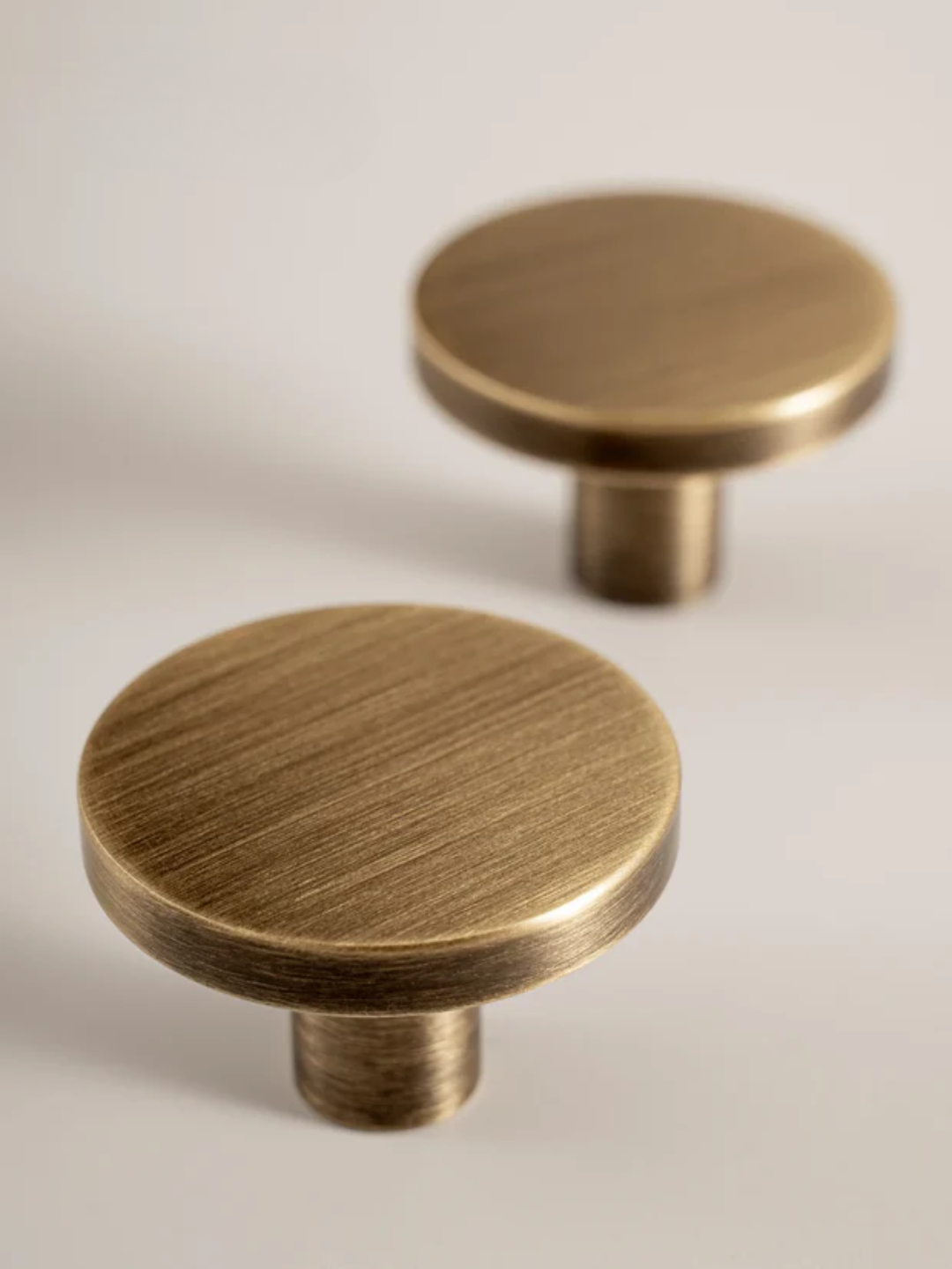 Two bronze cabinet knobs on a light beige background