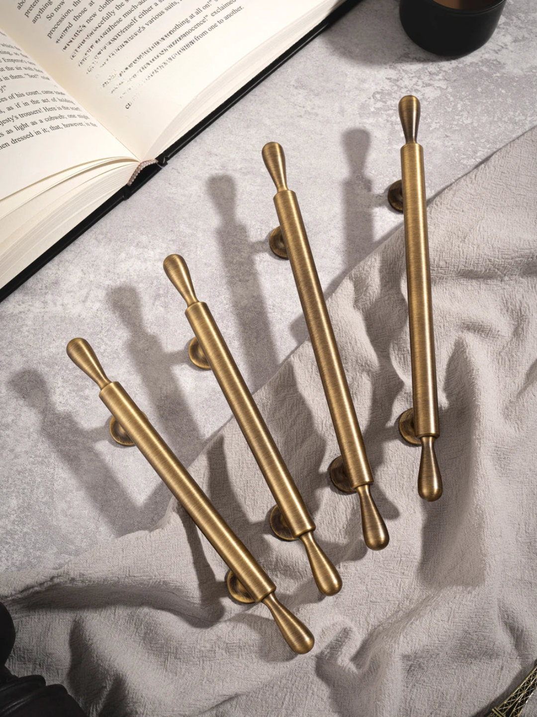 Set of gold cabinet handles on a textured surface with an open book in the background