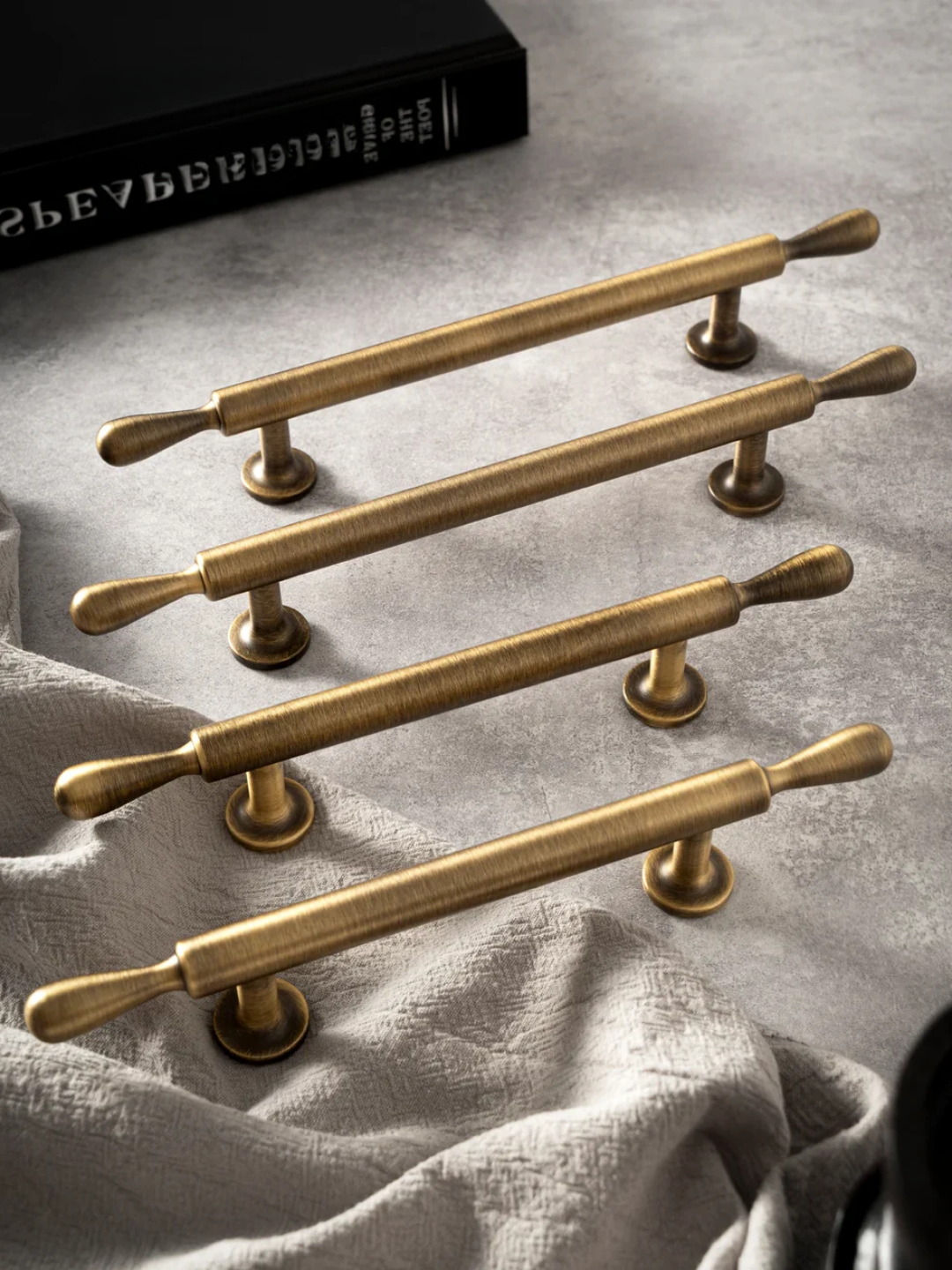 Set of gold cabinet handles on a textured surface with a book in the background