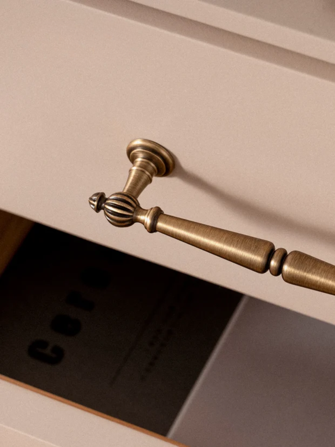 Close-up of a brass drawer handle on a light-colored cabinet.
