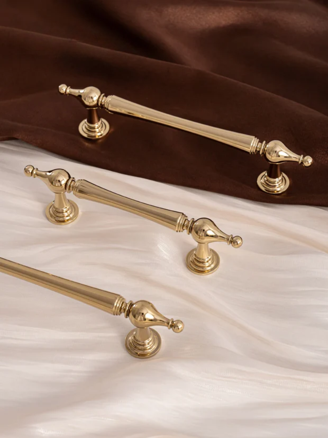 Set of gold cabinet handles on a brown and white fabric background