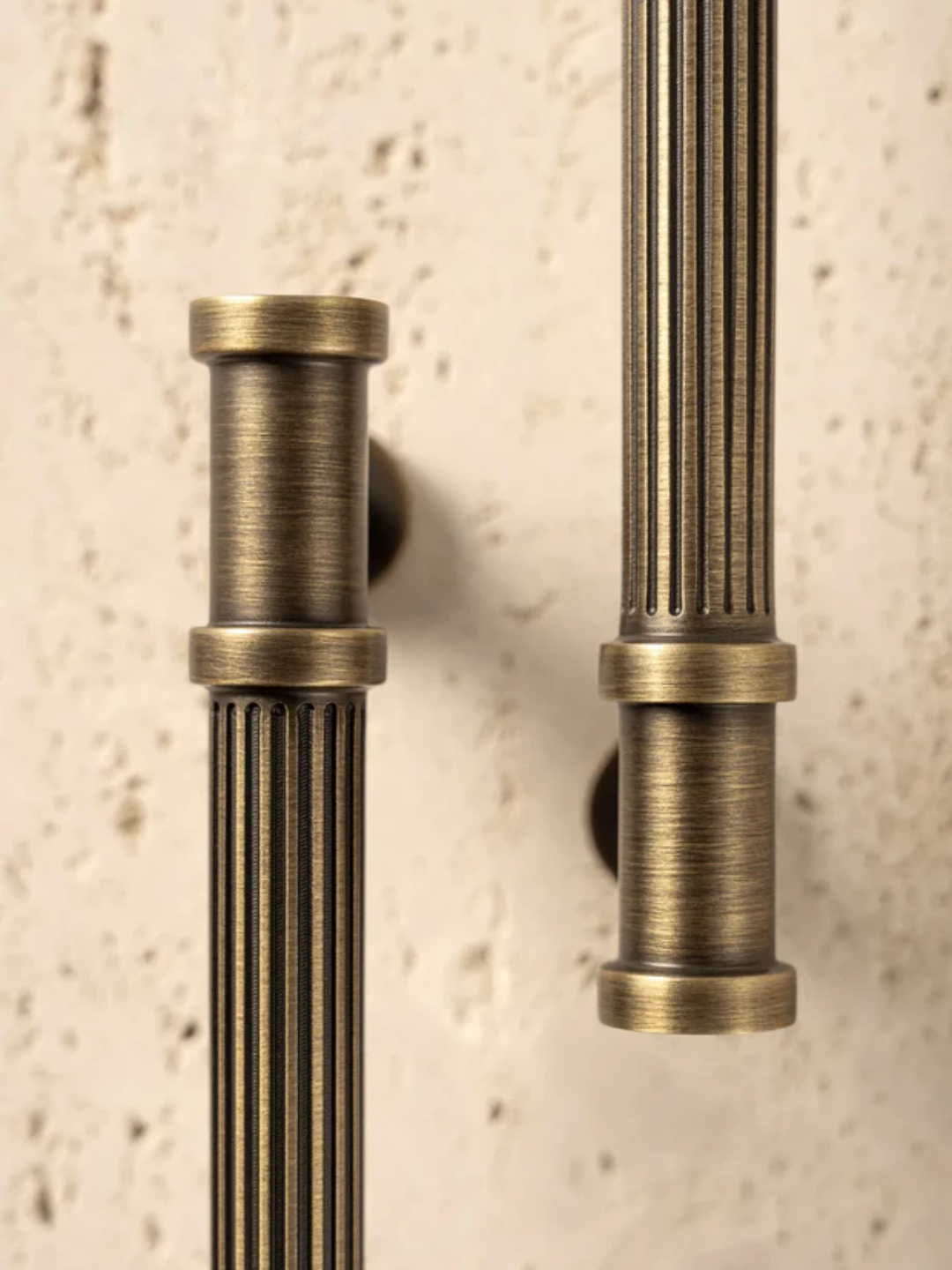 Close-up of two vintage-style bronze door handles on a textured beige wall.