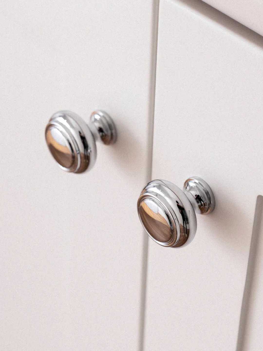 Chrome cabinet knobs on a white cabinet.