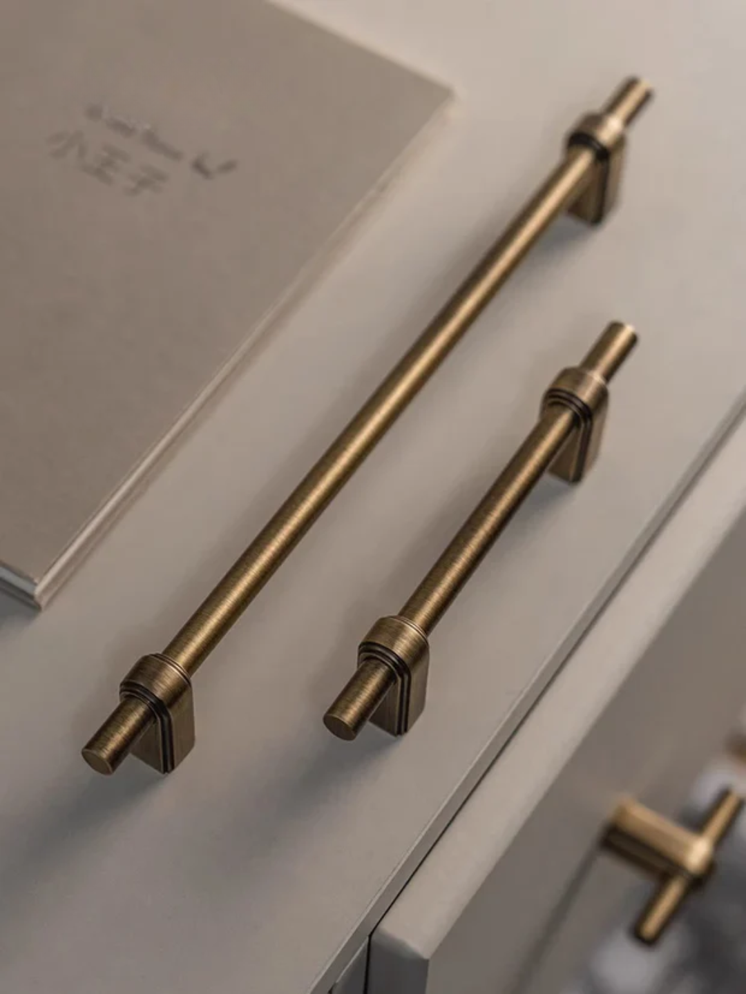 Brass cabinet handles on a light-colored surface with a book in the background.