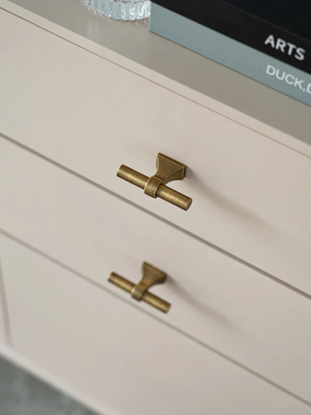 Close-up of a white drawer with brass handles on a light gray surface.