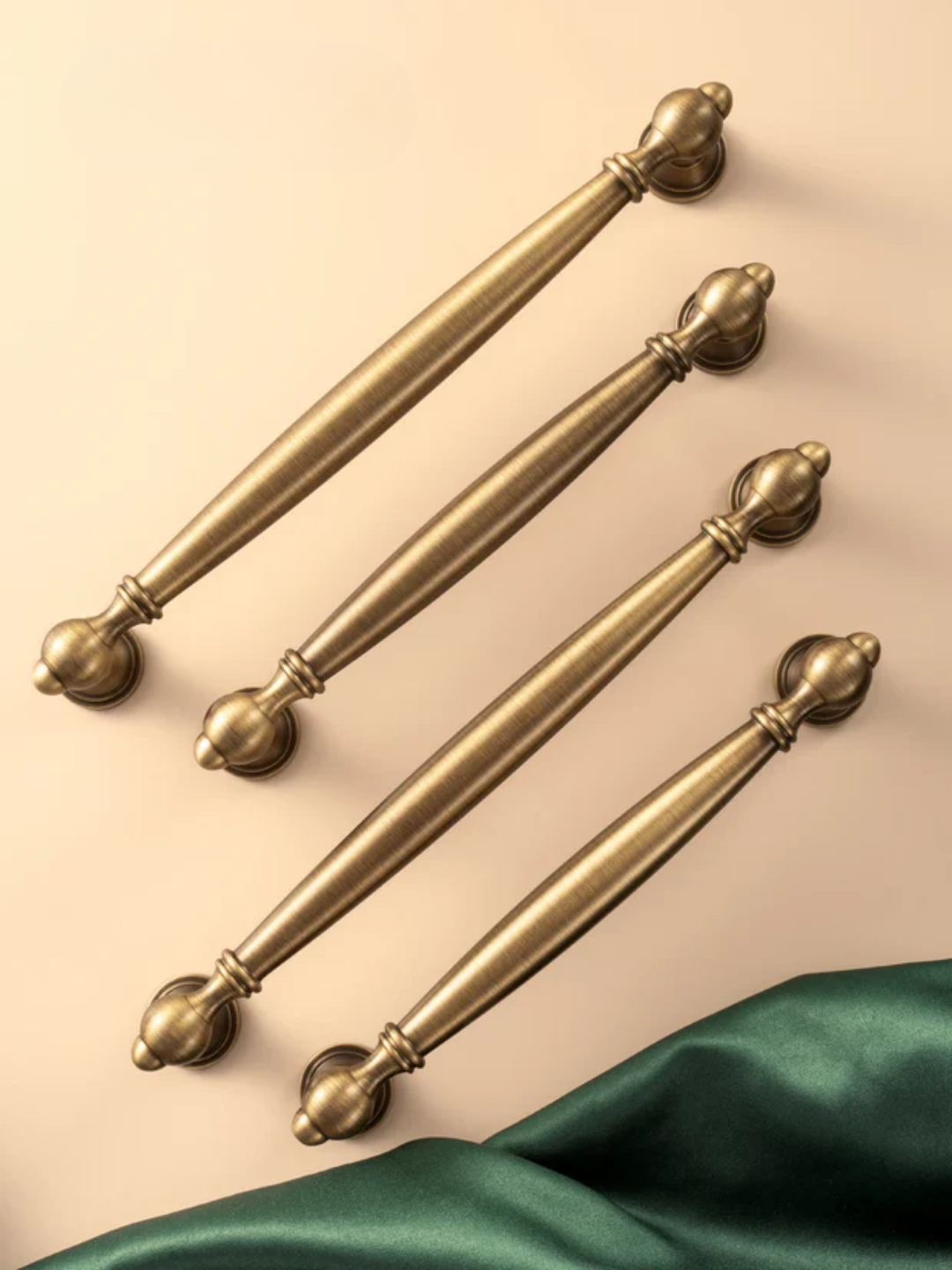Set of four gold handles on a beige background with a green fabric at the bottom.