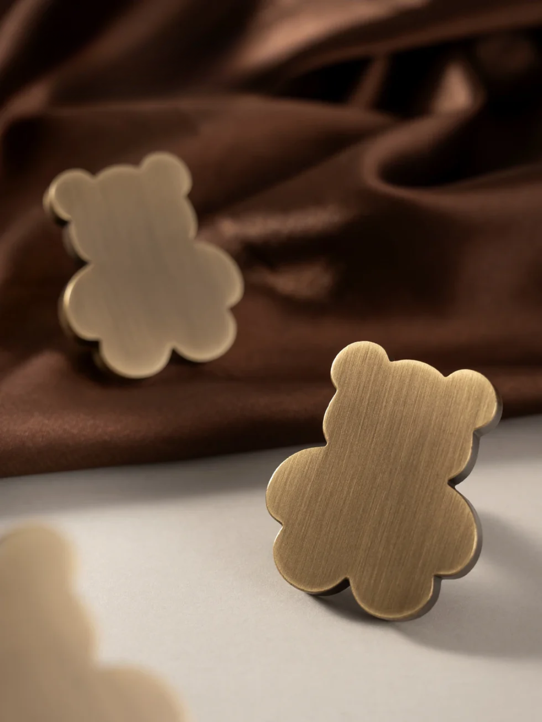 Gold teddy bear-shaped earrings on a brown fabric background