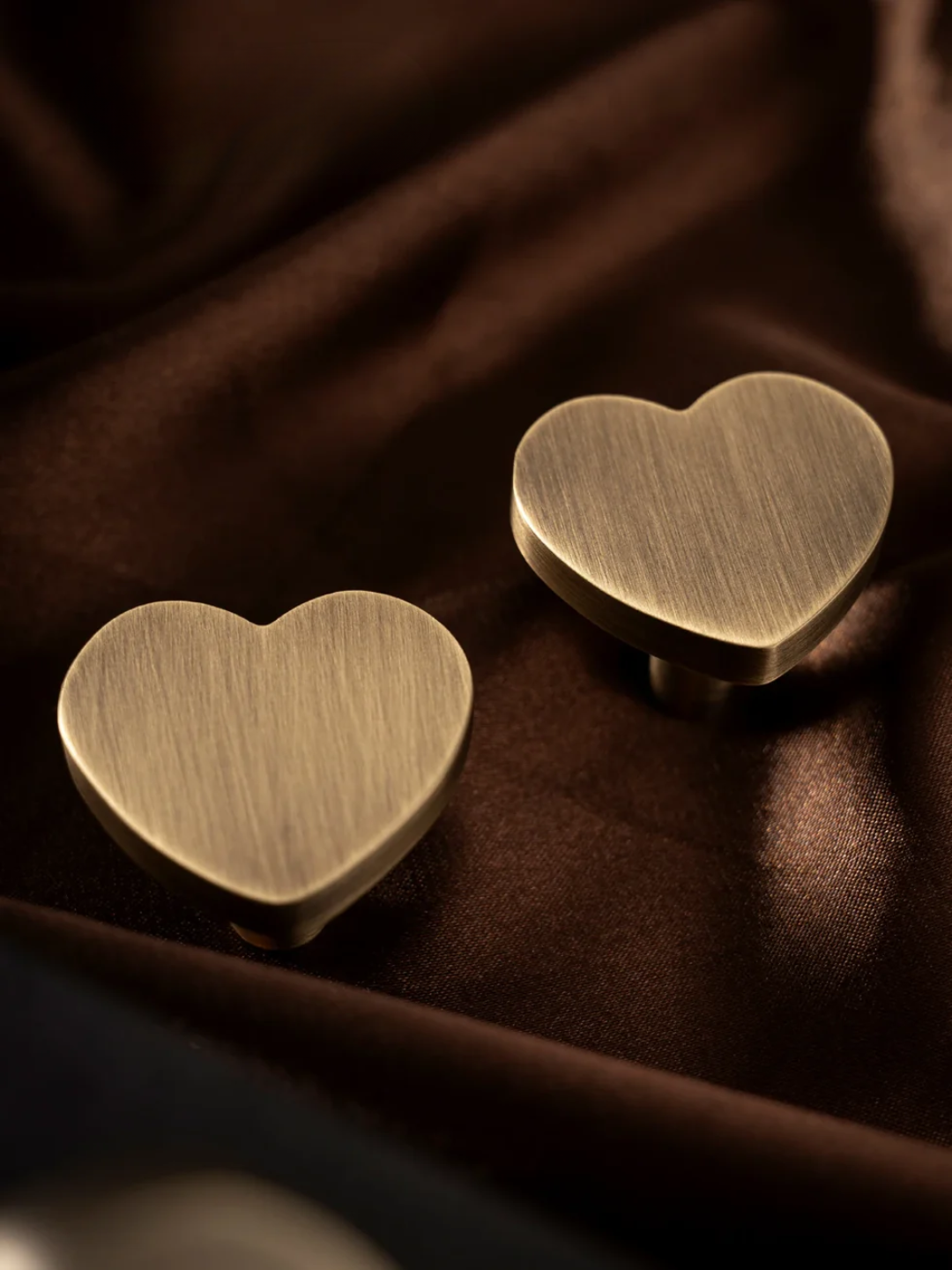 Two bronze heart-shaped objects on a brown fabric background