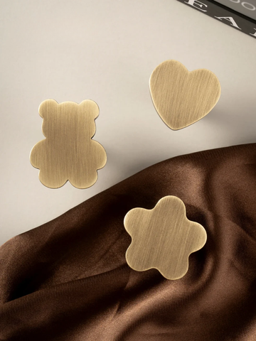 Gold heart and flower-shaped earrings on a brown fabric background