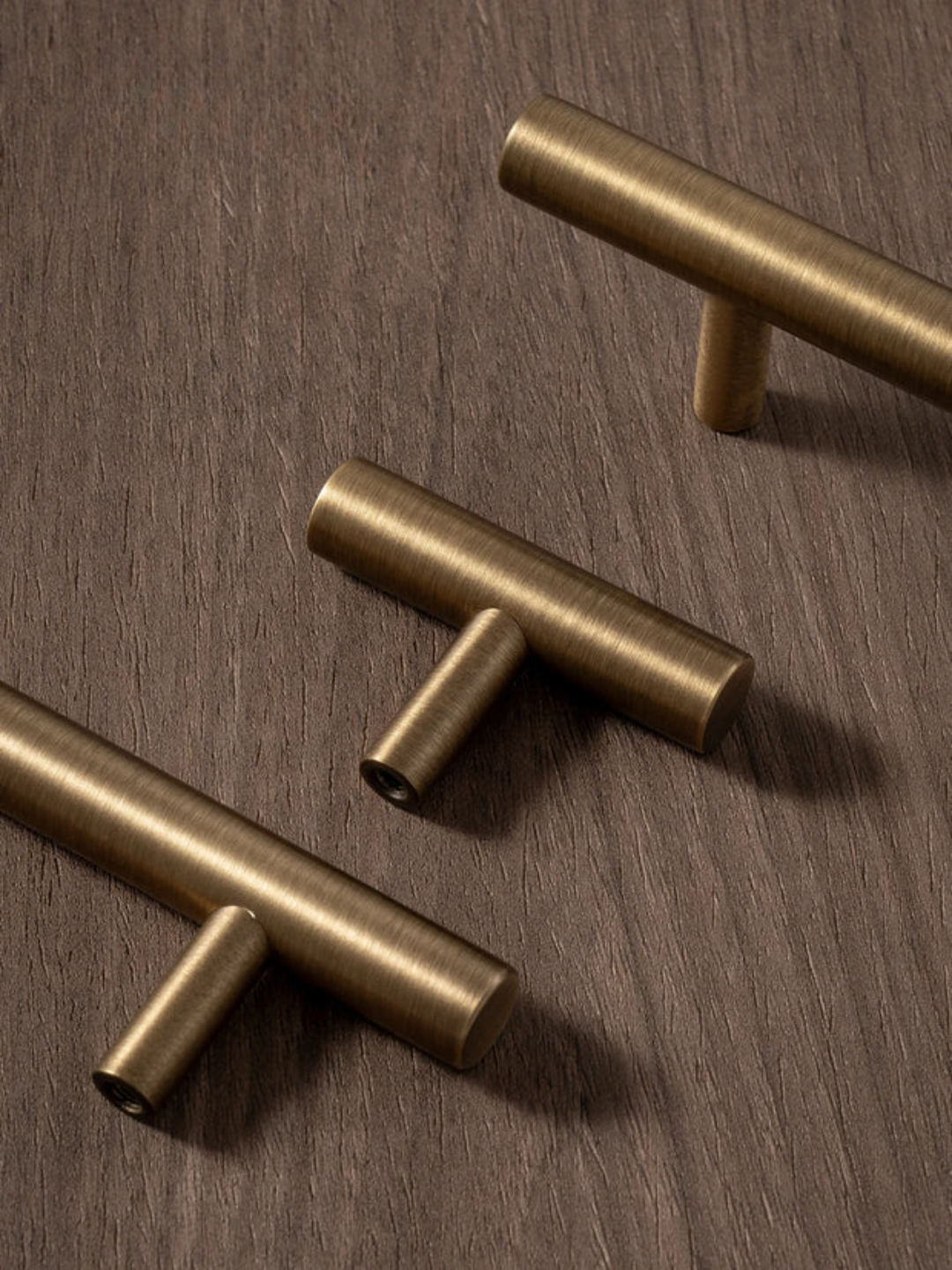 Three brass cabinet handles on a wooden surface