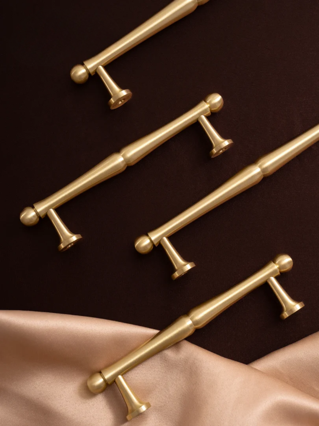 Set of gold cabinet handles on a dark surface with a satin fabric background