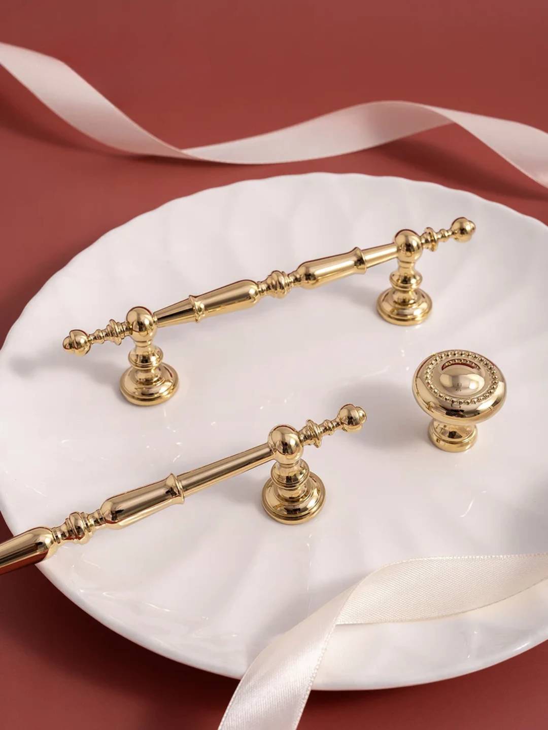 Gold hardware fixtures on a white plate with ribbons against a red background