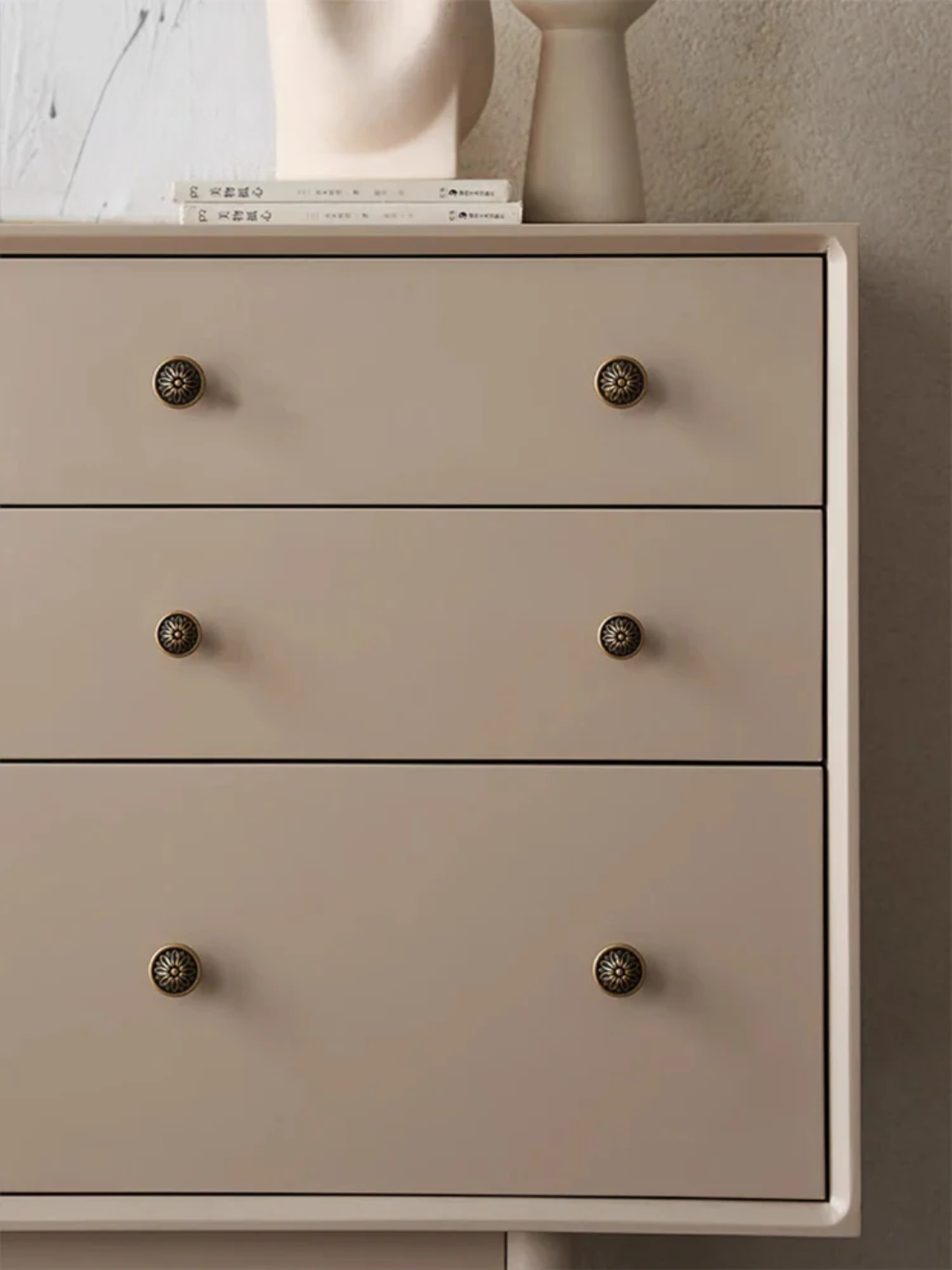 Beige dresser with four drawers and decorative knobs on a neutral background