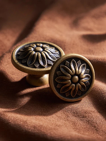 Two bronze flower-patterned cabinet knobs on a brown fabric background